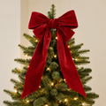 Large red velvet topper bow with two long tails draped over the top branches of a lit Christmas tree